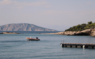 Amanzoe resort beach club overlooking calm Aegean waters and distant coastal cliffs.