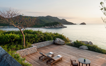 Ocean pool villa terrace at Amanoi with wooden deck, dining chairs, and views across calm waters to distant mountains.