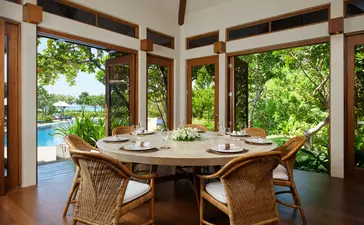 Salle à manger d'une villa quatre chambres à Amanpulo, avec table en bois et vues sur la végétation tropicale.