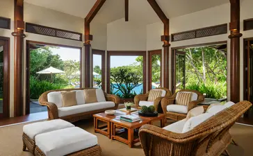 Lounge area in a four-bedroom villa at Amanpulo resort, with wooden beams, floor-to-ceiling windows overlooking tropical gardens, and contemporary furnishings.