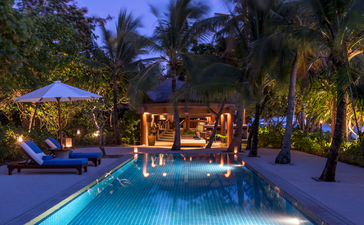 One-bedroom villa exterior at Amanpulo at dusk, with illuminated pool and palm-lined grounds.