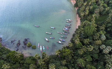 Aerial view of Amanpuri's coastal waters with moored boats and pristine sandy beach bordered by tropical vegetation.