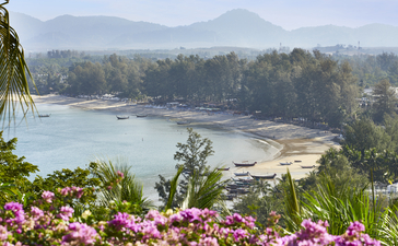Coastal view of Amanpuri with pink flowering plants in the foreground and turquoise waters beyond.