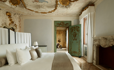 Alcova Tiepolo Suite principal bedroom at Aman Venice, with neutral walls, white bedding, and period architectural details.