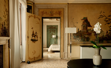 Alcova Tiepolo Suite living room at Aman Venice, with golden walls, classical artwork and fresh flowers in a ceramic vase.
