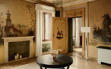 Salotto della suite Alcova Tiepolo ad Aman Venice, con camino acceso, pavimento in marmo e arredi chiari.