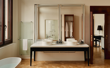Salle de bains avec fresques de l'appartement Coccinas à Aman Venice, dotée d'un lavabo noir et de miroirs élégants.