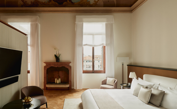 安缦威尼斯酒店卧室，配有木制床架、米色床上用品、古董家具和大窗户，采光充足。