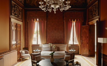 アマン ヴェニスのサンソヴィーノ・スタンツァ寝室。シャンデリア照明と赤褐色の壁に囲まれた優雅な空間。