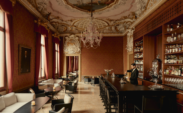 Bar at Aman Venice with terracotta walls, ornate ceiling, and shelves of spirits.