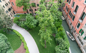Entrance courtyard with curved pathway and lush greenery at Aman Venice hotel.
