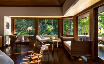 One-bedroom villa interior at Amanpulo with wooden furnishings and expansive windows overlooking tropical greenery.