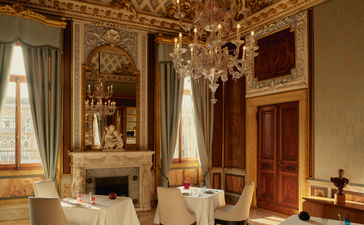 Ornate reception room at Aman Venice with gilt mirrors, crystal chandelier, and marble fireplace.