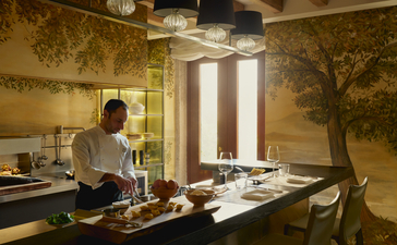Chef preparing food in the Palazzo kitchen at Aman Venice, with golden-toned walls and natural light from tall windows.