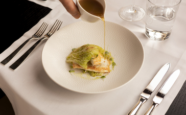 Arva dish plated at Aman Venice, featuring delicate green garnish on white porcelain with formal dining setup.