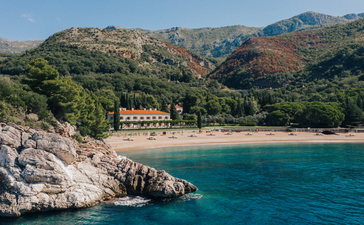 Villa Milocer's Kings Beach at Aman Sveti Stefan, with terracotta buildings nestled against forested hillsides and turquoise Adriatic waters.
