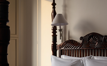 Sunlight streams through a sheer curtain beside a principal bedroom at Amangalla, illuminating a wooden cross on the bedside table.