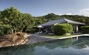 Amanoi residence with sloping roof reflected in plunge pool, surrounded by lush tropical landscape.