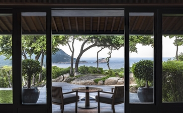 Amanoi residence terrace with wooden dining furniture overlooking coastal gardens and sea view.