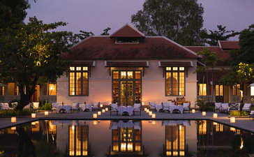Amantaka's wooden pavilion illuminated at dusk, reflected in still water with lanterns glowing around the pool.