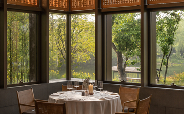 Dining area at Amanyangyun with round table, wooden chairs, and floor-to-ceiling windows overlooking gardens.