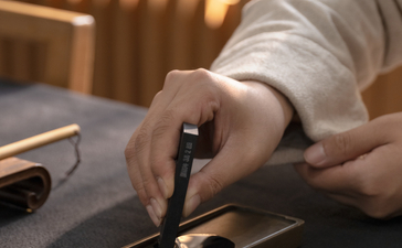 Hand holding a calligraphy brush over gold-leafed paper at Amanyangyun, China.