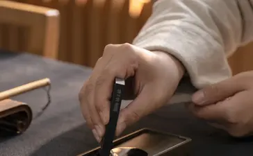 Hand holding a calligraphy brush over gold-leafed paper at Amanyangyun, China.