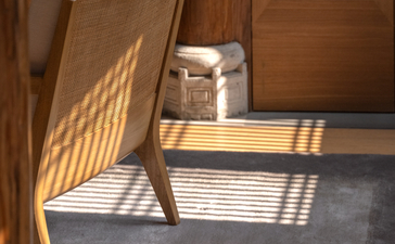 Sunlight streams across a wooden chair and slate floor at Amanyangyun, casting geometric shadows through a doorway.