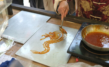 Chinese calligraphy demonstration at Amanyangyun, with brush and golden ink strokes on paper.