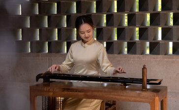 Woman playing guzheng traditional Chinese instrument at Amanyangyun, with decorative wall of woven baskets behind.