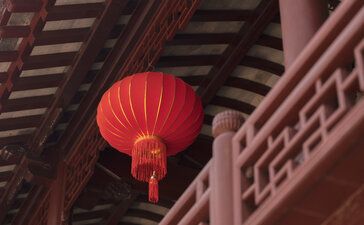 Red lantern hanging beneath wooden eaves at Amanyangyun, China.