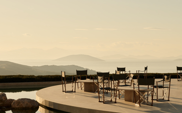 Exterior bar at Amanzoe with wooden deck overlooking still waters at dusk, Greece.
