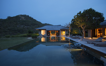 安缦诺怡度假村临水建筑在黄昏时分亮起灯光，倒影映入平静水面。