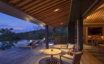 Covered terrace at Amanoi with wooden ceiling overlooking illuminated pool and landscape at dusk.