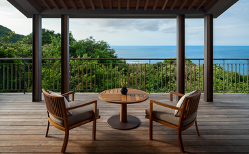 Wooden terrace at Amanoi with two chairs and table overlooking tropical vegetation and blue sea.