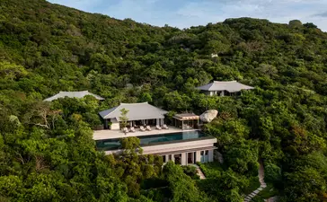 Amanoi resort nestled among verdant hillsides, aerial view showing contemporary architecture integrated within lush tropical landscape.