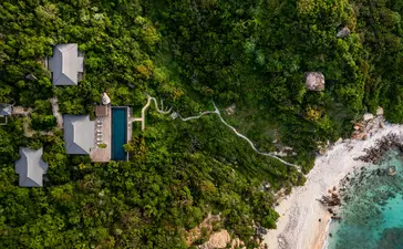 Amanoi resort viewed from above, with pavilions nestled amongst dense green forest meeting a turquoise coastline.