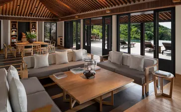 Amanoi resort living pavilion with wooden dining table, upholstered seating, and garden views through glass doors.