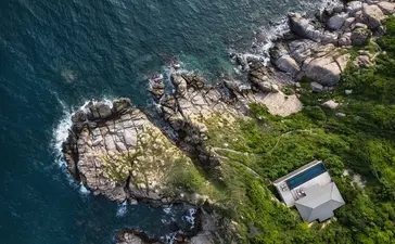 Amanoi cliffside villa overlooks rocky coastline and turquoise waters below.