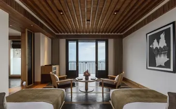 Amanoi suite with wooden ceiling, seating area, and views towards the landscape beyond floor-to-ceiling windows.