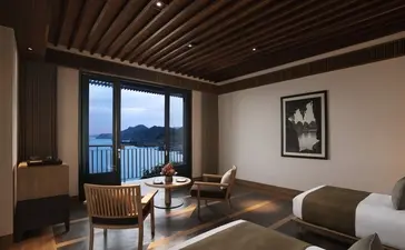 Principal bedroom at Amanoi with wooden ceiling, floor-to-ceiling windows overlooking the coast, and contemporary furnishings.