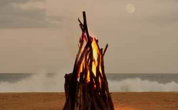 Feu de plage au coucher du soleil à Amanera, avec bois empilés sur le sable face à l'océan.