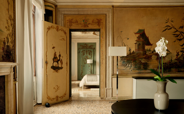 Alcova Tiepolo Suite living room at Aman Venice, with warm wood panelling, doorway to bedroom, and fresh flowers in vase.