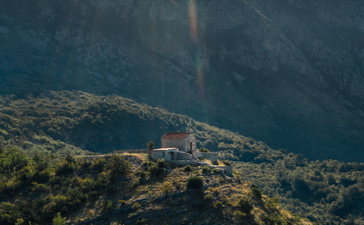 Aman Sveti Stefan set against forested Montenegrin mountains under soft afternoon light.