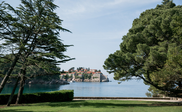 Aman Sveti Stefan's islet visible across turquoise Adriatic waters, framed by pine trees.