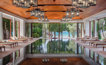 Symmetrical spa corridor at Aman Sveti Stefan with reflecting pool, pink walls, and sea views through central columns.
