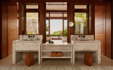 Cuarto de baño con doble lavamano, espejos de madera y taburetes en Amanera resort.