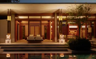 Amanera resort's evening exterior with warm-lit pavilion reflected in still water at dusk.
