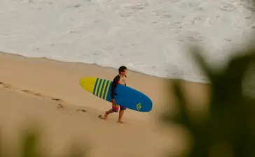 Surfer holding board on sandy beach at Amanera resort.