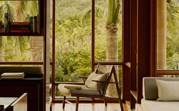 Bibliothèque du resort Amanera avec fauteuil en bois près de grandes fenêtres donnant sur la forêt dominicaine.
